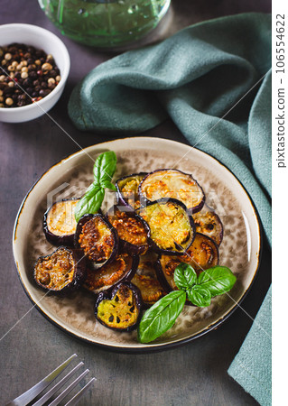 Pieces of fried eggplant with spices and basil on a plate on the table vertical view Pieces of fried eggplant with spices and basil on a plate on the table vertical view 106554622