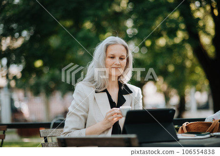 Portrait of beautiful female manager in middle age with gray hair working outdoors. Portrait of beautiful female manager in middle age with gray hair working outdoors. 106554838
