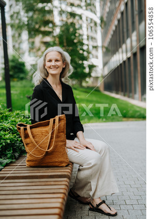 Portrait of beautiful woman with gray hair sitting on bench in city. Portrait of beautiful woman with gray hair sitting on bench in city. 106554858