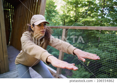 Happy mid adult woman doing exercise outdoors on terrace of tree house, weekend away and digital detox concept. Happy mid adult woman doing exercise outdoors on terrace of tree house, weekend away and digital detox concept. 106554862