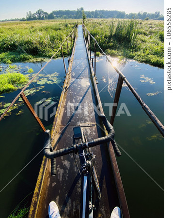 faceless cyclist stands on a village bridge over a lake overgrown with 106556285