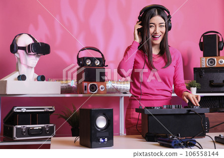 Cheerful musician standing at dj table mixing electronic music with techno using professional mixer console, having fun in studio over pink background. Artist playing stereo sounds with electronics Cheerful musician standing at dj table mixing electronic music with techno using professional mixer console, having fun in studio over pink background. Artist playing stereo sounds with electronics 106558144
