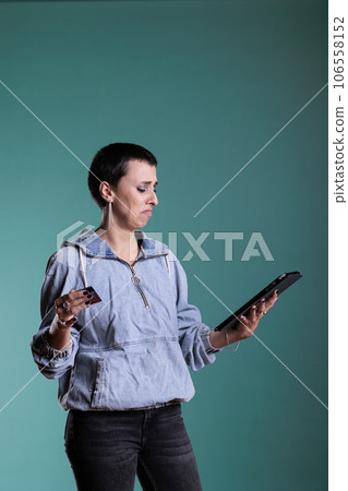 Worried preoccupied woman doing online shopping holding tablet computer while typing credit card details having difficulties after seeing the prices. Concerned female ordering expensive products Worried preoccupied woman doing online shopping holding tablet computer while typing credit card details having difficulties after seeing the prices. Concerned female ordering expensive products 106558152