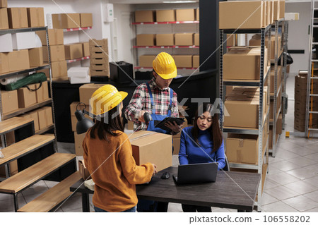 Storehouse managers team scanning parcel and checking information on laptop. Asian warehouse operators colleagues controlling cardboard box shipment at storage office desk 106558202