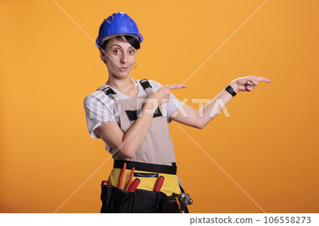 Confident handywoman pointing left or right sides, showing sideways and indicating direction in studio. Builder with helmet posing aside over background, renovation project service. Confident handywoman pointing left or right sides, showing sideways and indicating direction in studio. Builder with helmet posing aside over background, renovation project service. 106558273