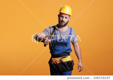 Construction worker using hammer on renovation project, standing over yellow background. Professional male renovator doing reconstruction work with sledgehammer and tools, studio shot. Construction worker using hammer on renovation project, standing over yellow background. Professional male renovator doing reconstruction work with sledgehammer and tools, studio shot. 106558297