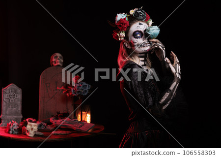 Santa muerte goddess wearing flowers crown and holding beautiful rose, looking glamour in mexican halloween costume. Celebrating dios de los muertos with tranditional festival make up. Santa muerte goddess wearing flowers crown and holding beautiful rose, looking glamour in mexican halloween costume. Celebrating dios de los muertos with tranditional festival make up. 106558303