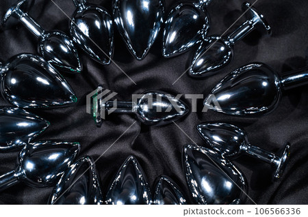 Many metal anal plugs on a black silk sheet. Many metal anal plugs on a black silk sheet. 106566336