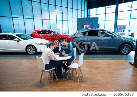 Happy caucasian couple signs a contract for the purchase of a car salon. Happy caucasian couple signs a contract for the purchase of a car salon. 106566338