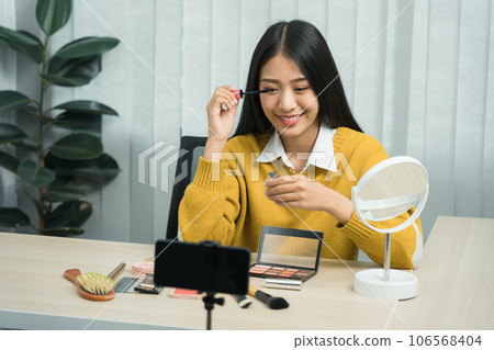 Young asian woman vlogging herself about beauty products with making a video for her blog on cosmetics using phone camera at home. 106568404