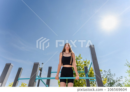 A young woman is doing an exercise on the horizontal bar outdoor. 106569604
