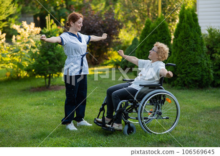 A nurse is exercising with an elderly patient in a wheelchair outdoors. A nurse is exercising with an elderly patient in a wheelchair outdoors. 106569645