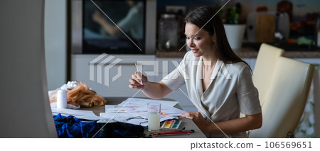 Woman drawing sketches of swimwear and underwear in watercolor while sitting in the kitchen.  106569651