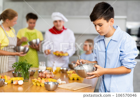 Cooking course - portrait of teenage boy in an apron who is learning to beat eggs to make pancakes at cooking class 106570046