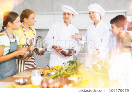 Young guy and adult woman cook teaches group of children to cook 106570079