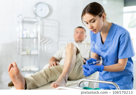 Young woman doctor doing knee injection for the patient lying on clinical chair Young woman doctor doing knee injection for the patient lying on clinical chair 106570213