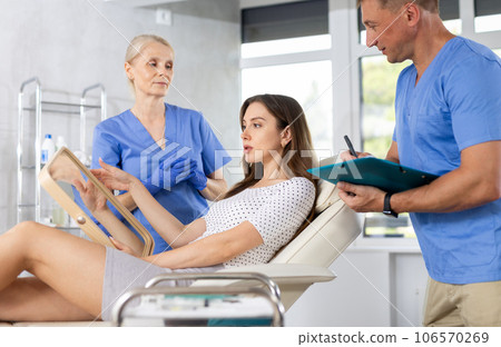 Elderly lady dermatologist examines skin of womans face, male nurse records data in client card 106570269