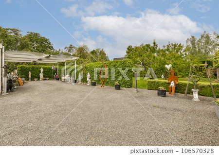 an outdoor area with various plants and sculptures on the ground in front of a house under a blue sky filled with white clouds an outdoor area with various plants and sculptures on the ground in front of a house under a blue sky filled with white clouds 106570328