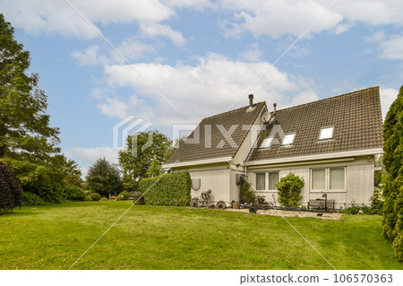 a small house in the middle of a grassy area with trees and bushes on either side of the house there is a blue sky a small house in the middle of a grassy area with trees and bushes on either side of the house there is a blue sky 106570363
