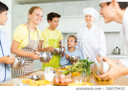 While cooking classes, teen girl stands on other side of table from cook guy and looks at him 106570432