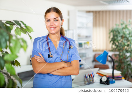 Confident young female doctor in blue uniform standing in office 106570433