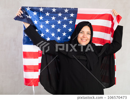 Happy young woman dressed in traditional islamic clothes with american flag Happy young woman dressed in traditional islamic clothes with american flag 106570473