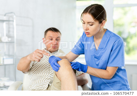 Man client of clinic looks at specialist and tells to woman doctor where knee hurts 106570477