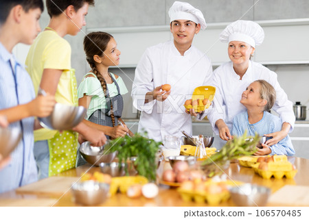 During cooking lesson, male cook tells children about culinary rules, woman assistant helps child 106570485