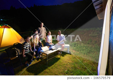 People enjoying an outdoor theater with a projector at a camp 106570579