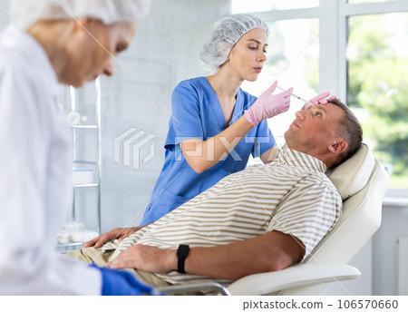 Woman cosmetologist making injections in forehead to adult man Woman cosmetologist making injections in forehead to adult man 106570660