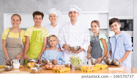 Young guy and adult woman cook pose with group of children at master class Young guy and adult woman cook pose with group of children at master class 106570737