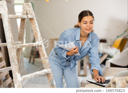 Smiling woman architect using laptop during repair works 106570823