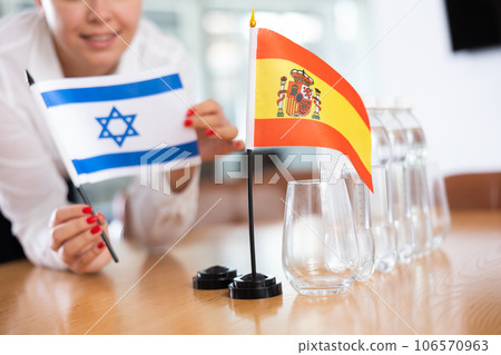 Unrecognizable girl sets midget flags of Spain and Israel before international negotiations 106570963