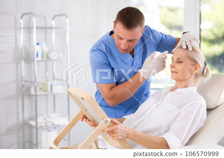 Senior woman looking at mirror while cosmetologist explaining facial procedure Senior woman looking at mirror while cosmetologist explaining facial procedure 106570999