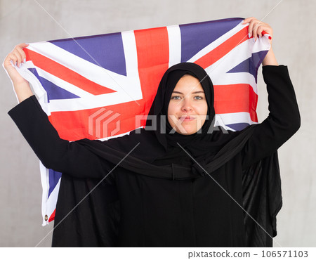 Happy young woman dressed in traditional islamic clothes with british flag 106571103