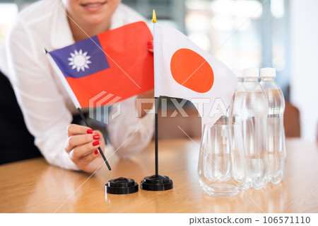 Female hands placing flags of Taiwan and Japan on table before meeting 106571110