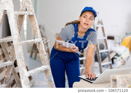 Portrait of a female builder who checks the work done using laptop Portrait of a female builder who checks the work done using laptop 106571120