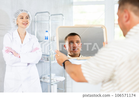 Man looks in mirror and rejoices at successful treatment of dermatological problems of face 106571174