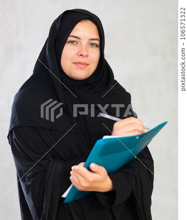 Cheerful young muslim student dressed in black hijab holding textbooks Cheerful young muslim student dressed in black hijab holding textbooks 106571322