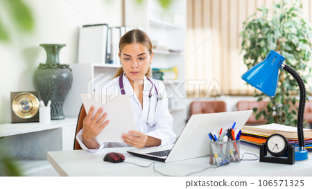 Young woman doctor studies the patient's outpatient card while sitting at a computer in the office Young woman doctor studies the patient's outpatient card while sitting at a computer in the office 106571325