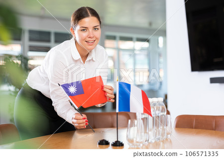 Young woman putting flags of Taiwan and France on table in office 106571335
