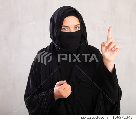 Young woman dressed in traditional islamic clothes with her face covered pointing to something 106571345
