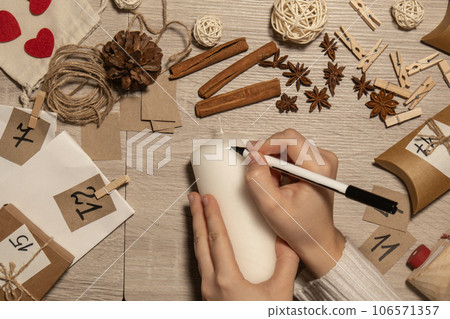 Unrecognizable young woman paint numbers on candles. Female making homemade advent calendar Made with your own hands step by step DIY crafts do it yourself. Preparation to christmas concept. Seasonal 106571357
