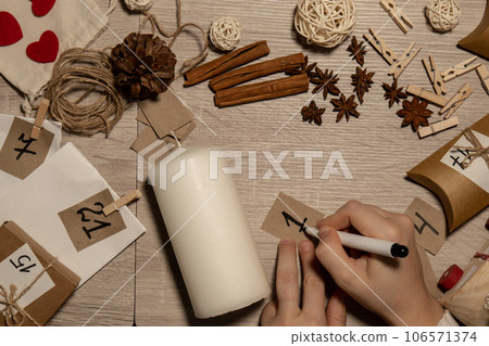 Unrecognizable young woman paint numbers on candles. Female making homemade advent calendar Made with your own hands step by step DIY crafts do it yourself. Preparation to christmas concept. Seasonal 106571374