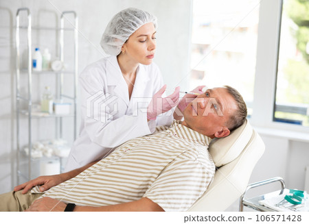 Professional cosmetologist in gloves performs a procedure on cosmetology operation of man face in clinic 106571428