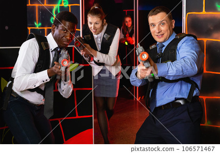 Men and women in business suits playing laser tag emotionally in dark room 106571467