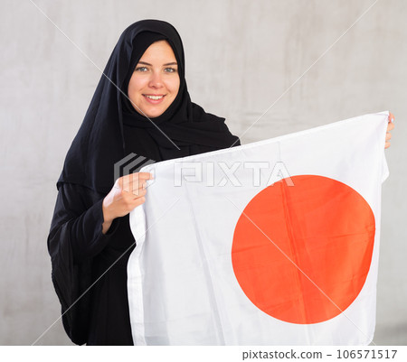 Smiling joyful Muslim woman in traditional black hijab holds flag of Japan 106571517