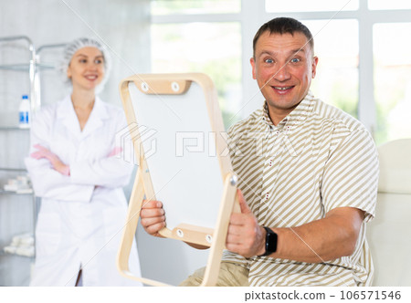 Satisfied man examines his face in mirror after plastic surgery 106571546