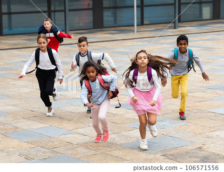 Happy tween schoolchildren with backpacks running to school outdoors Happy tween schoolchildren with backpacks running to school outdoors 106571556