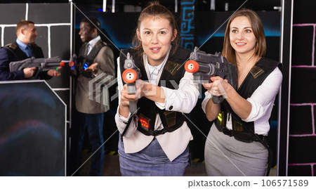 Portrait of two women in business suits playing laser tag with co-workers 106571589